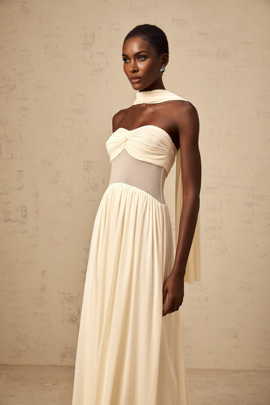 A woman wearing a neutralcolored midi dress with a scarfinspired mesh design featuring flowy fabric and delicate patterns