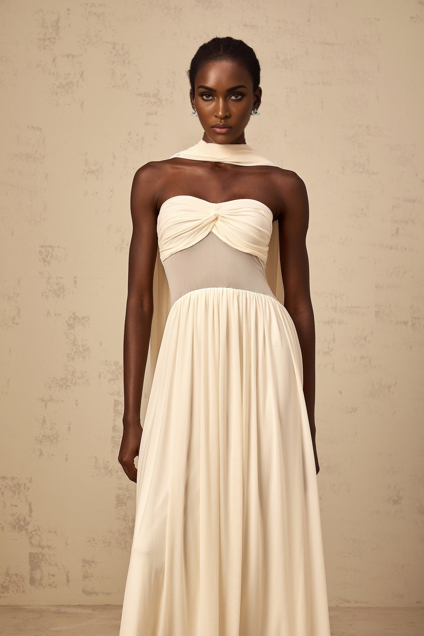 A woman wearing a neutralcolored midi dress with a scarfinspired mesh design featuring intricate patterns and a flowing silhouette