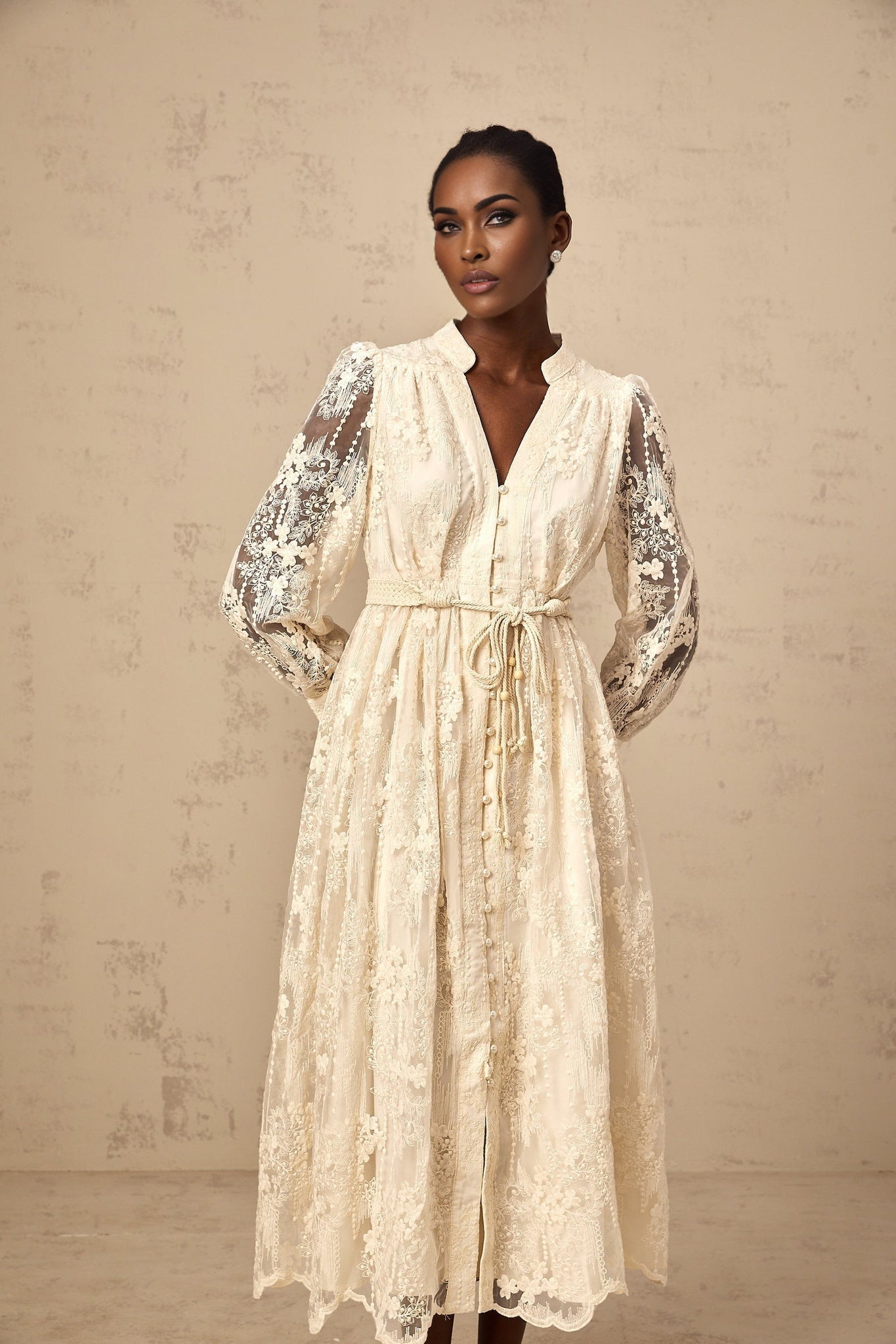 A woman wearing a neutralcolored midi dress with lace embroidery details standing in a relaxed pose