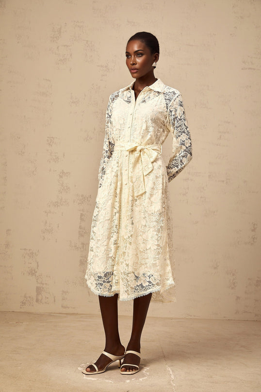 A woman wearing a neutralcolored midi shirt dress with delicate guipure lace detailing standing in a relaxed pose against a plain background