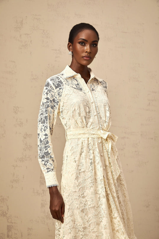 A woman wearing a neutralcolored midi shirt dress with guipure lace detailing standing against a plain background