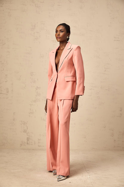 A woman wearing a pink blazer and trousers set with embroidery details and cutout designs The blazer features a tailored fit while the trousers are slim The set is adorned with delicate floral embroidery in contrasting colors Cutout elements add a modern touch to the ensemble
