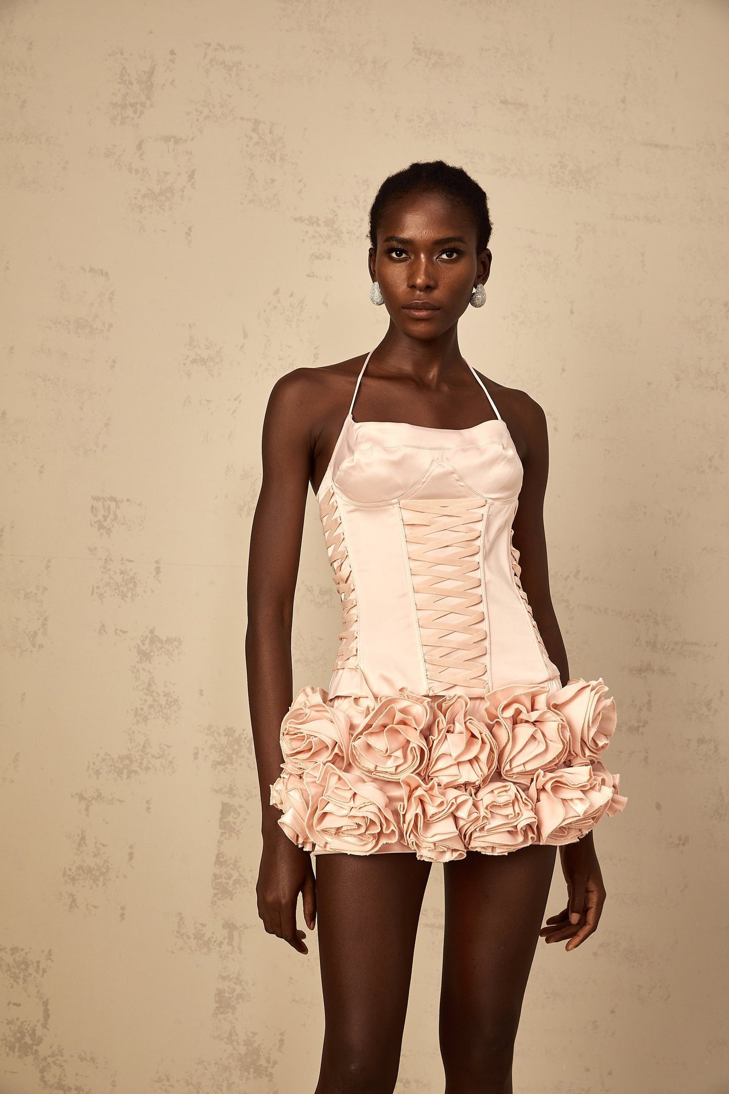 A woman wearing a pink matching set consisting of a lace up top and skirt adorned with faux flower details