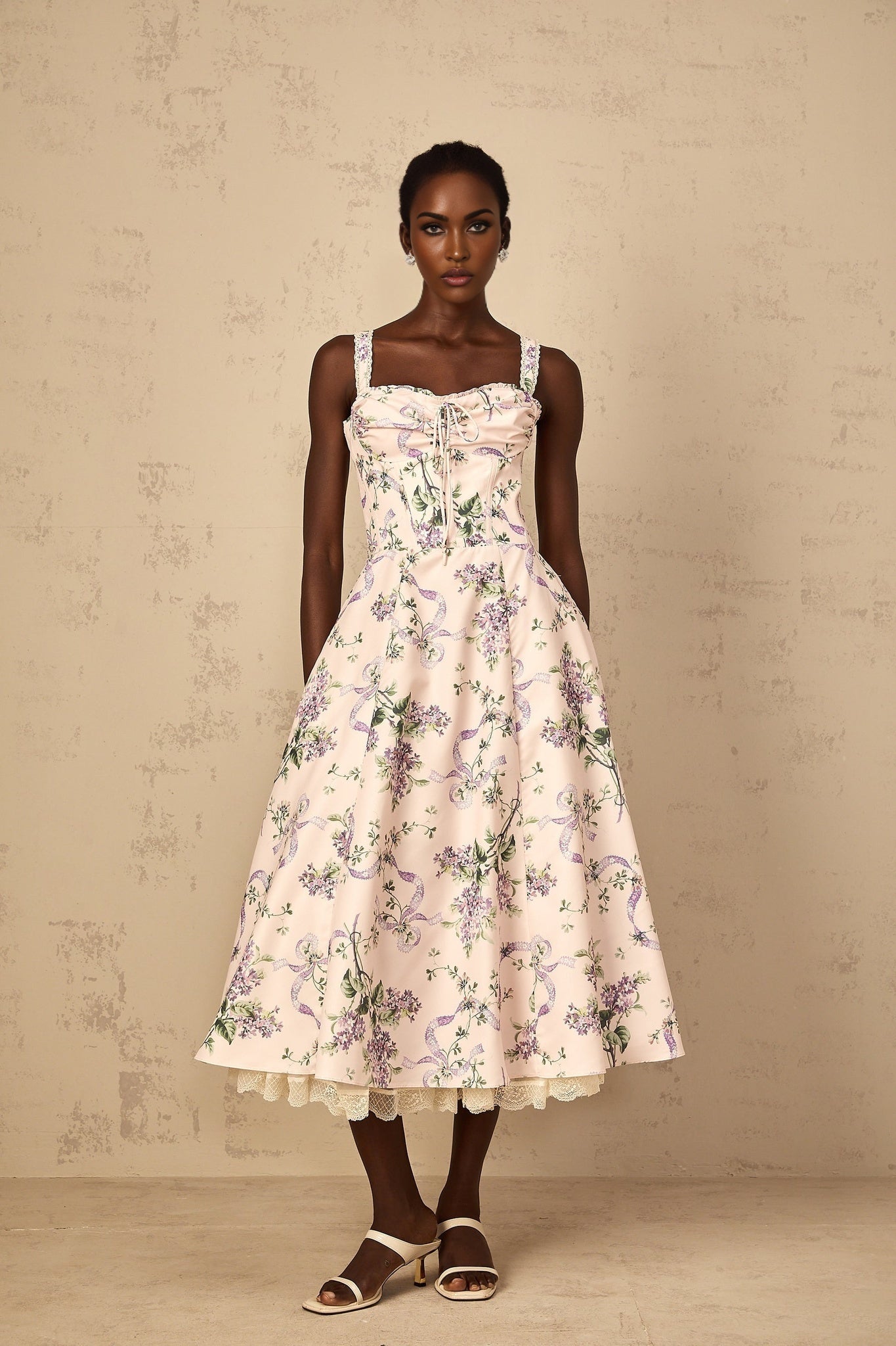 A woman wearing a pink midi dress with a floral print and shirred detailing
