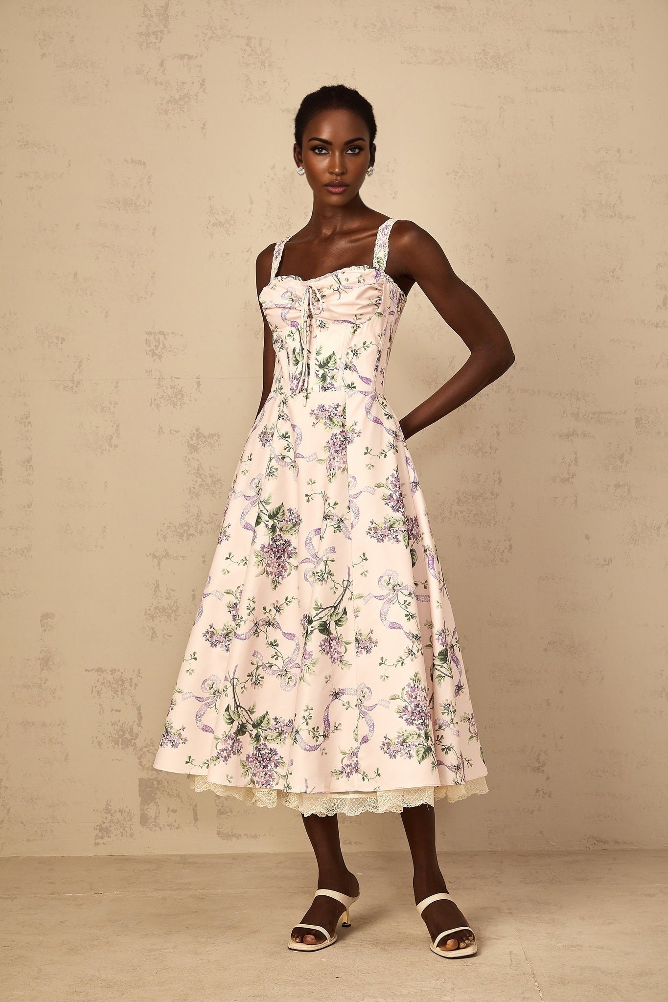 A woman wearing a pink midi dress with a floral print and shirred details