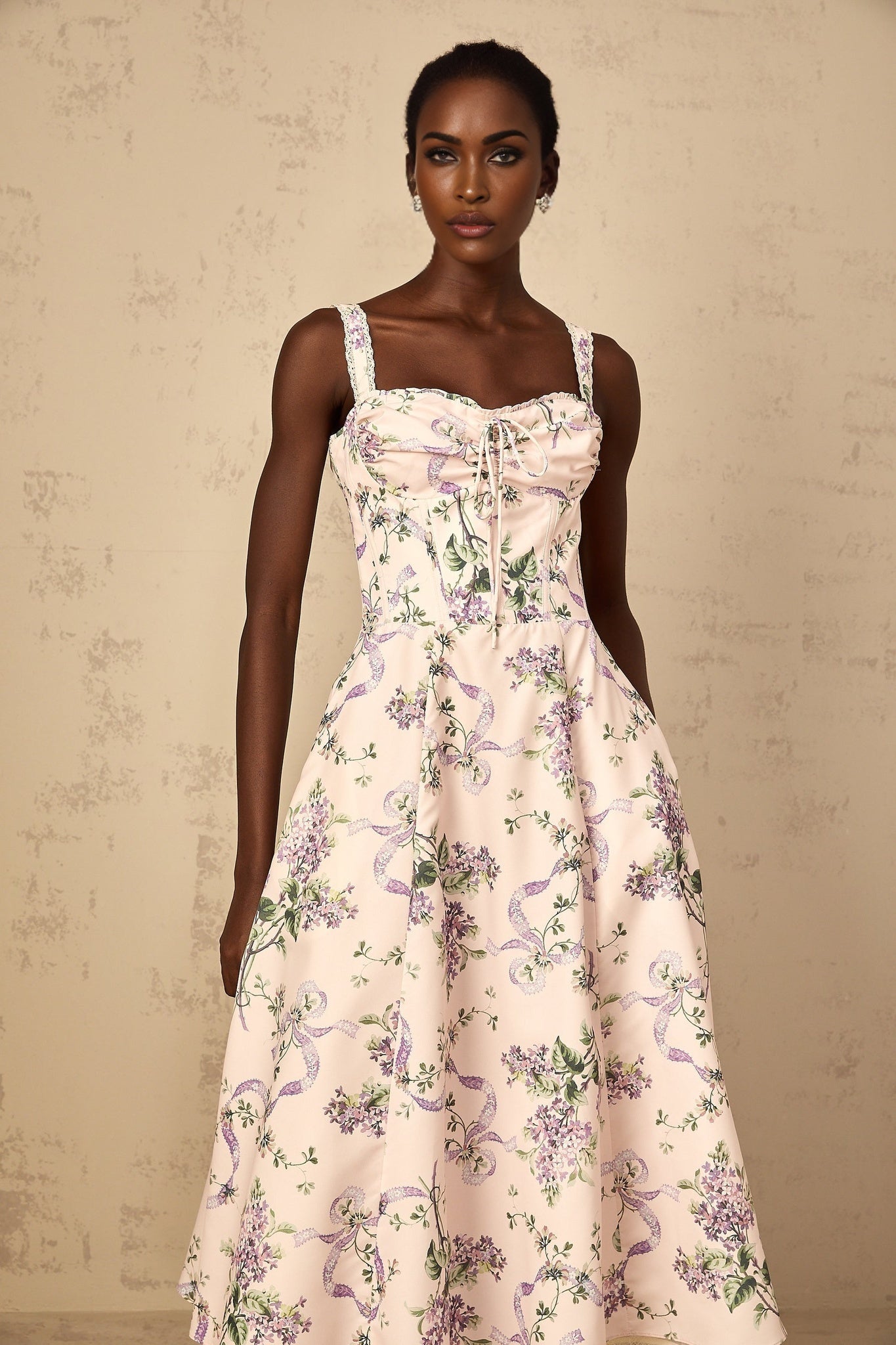 A woman wearing a pink midi dress with a floral print pattern and shirred detailing