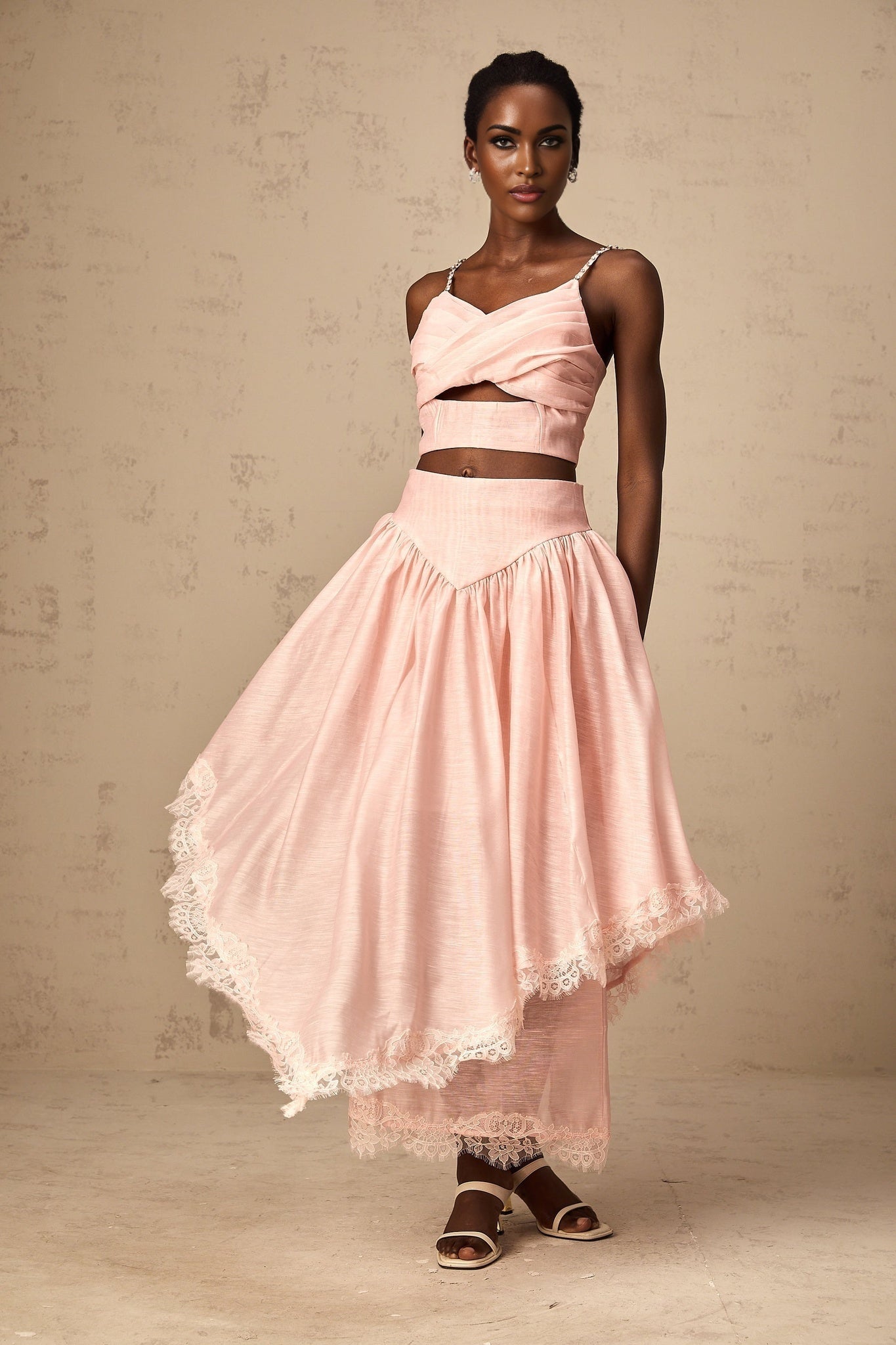 A woman wearing a pink twopiece outfit consisting of an asymmetric ruffled top and matching skirt set