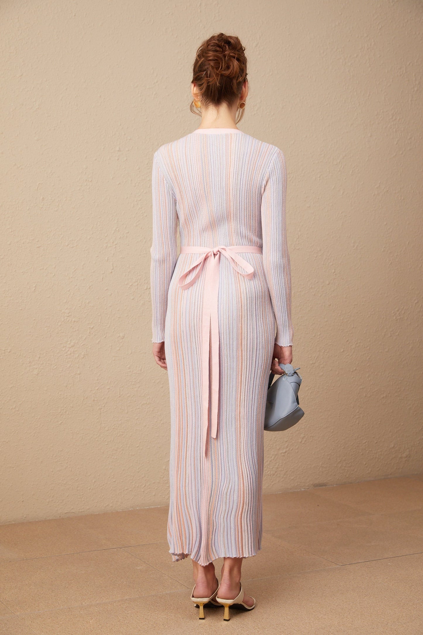A woman wearing a pleated knit midi dress with a V neckline in a soft color standing against a plain background