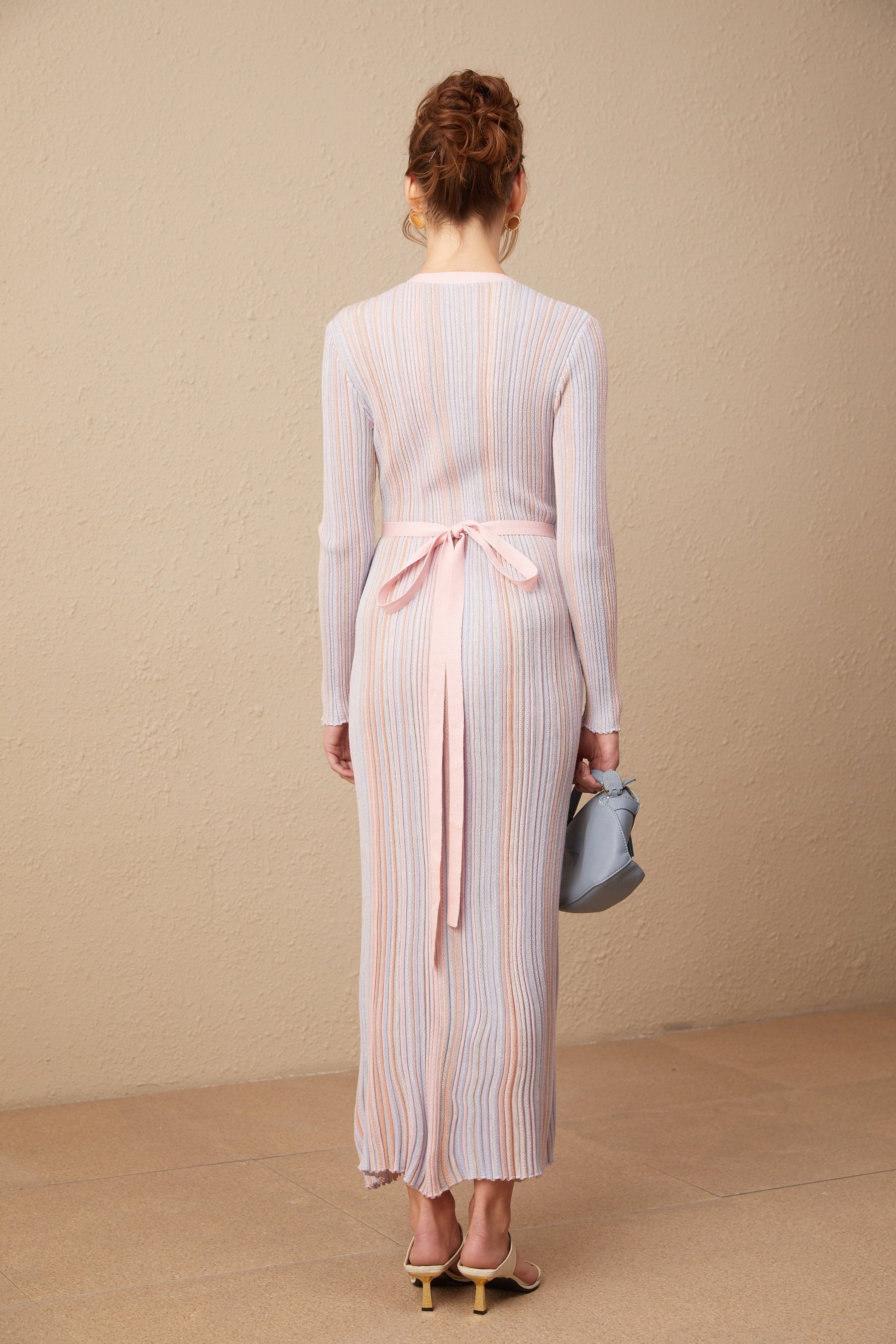 A woman wearing a pleated knit midi dress with a V neckline in a soft color standing against a plain background
