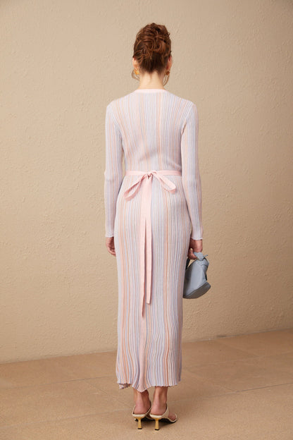 A woman wearing a pleated knit midi dress with a V neckline in a soft color standing against a plain background