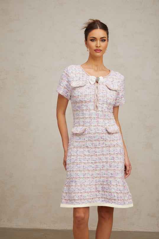 A woman wearing a purple and white checked knit midi dress with long sleeves and a fitted silhouette standing against a plain background