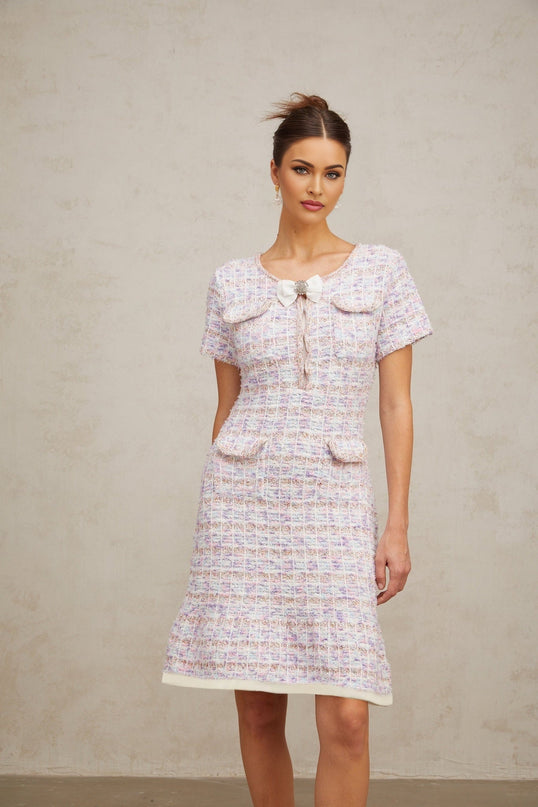 A woman wearing a purple and white checked knit midi dress with long sleeves and a fitted silhouette standing against a plain background