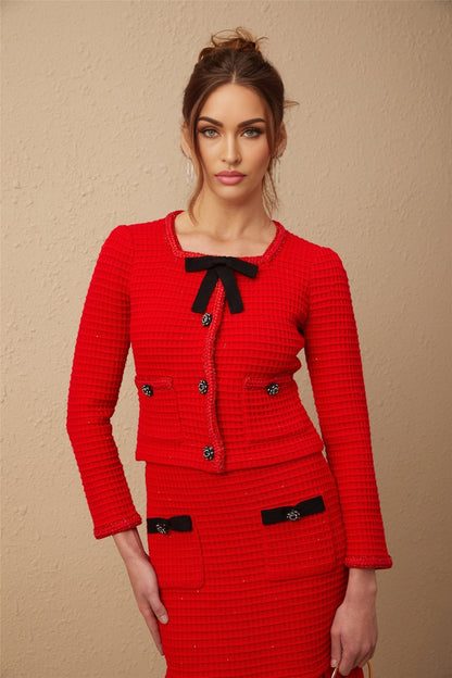 A woman wearing a red braided waffle knit jacket and matching skirt set standing in a neutral pose