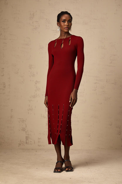 A woman wearing a red knitted midi dress with long sleeves and beaded details The dress features cutout sections and falls to mid calf length