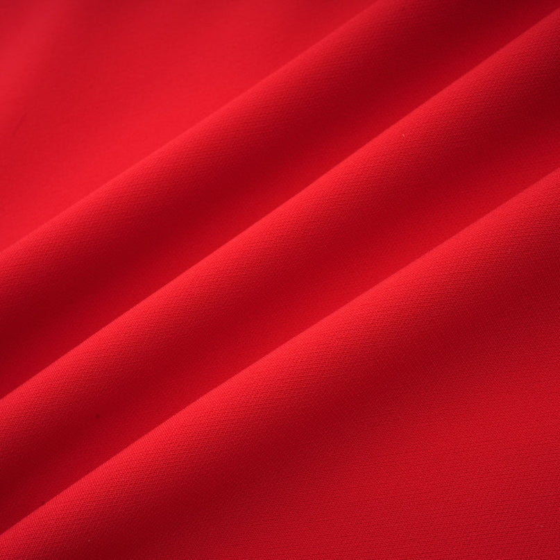 A woman wearing a red long sleeve dress with a floral pattern standing against a plain background