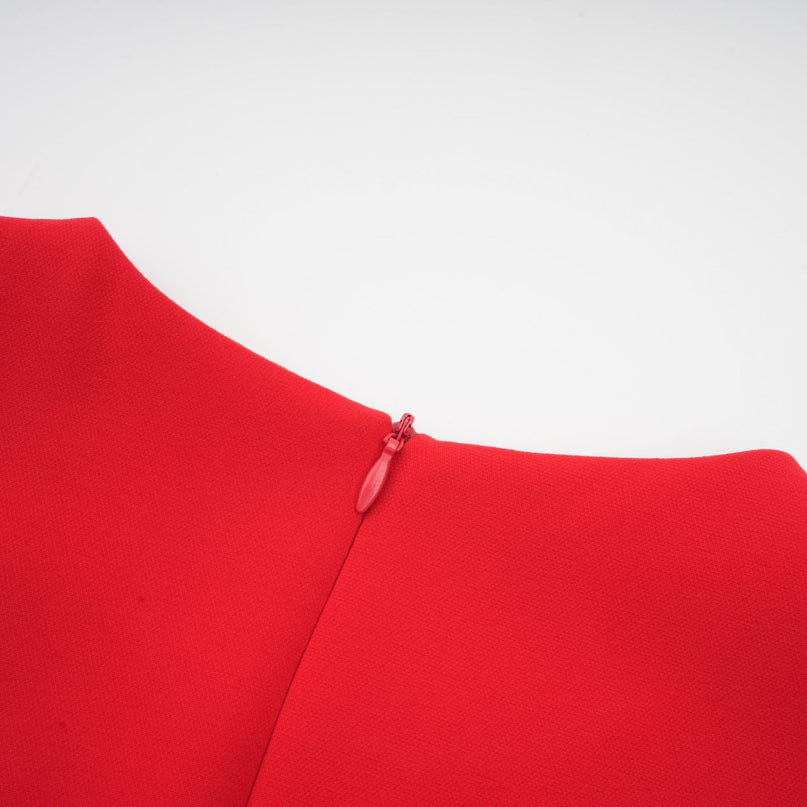 A woman wearing a red long sleeve dress with a floral pattern standing against a plain background