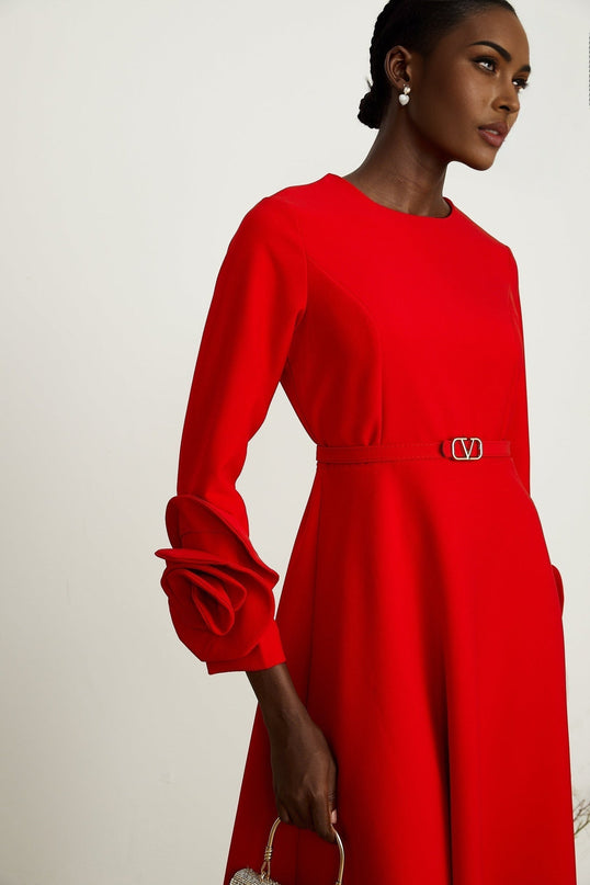 A woman wearing a red long sleeve dress with a floral pattern standing against a plain background