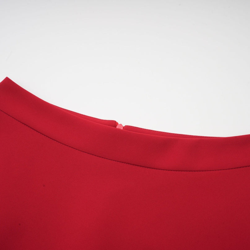 A woman wearing a red pleated blouse paired with a matching red pleated skirt standing against a plain background