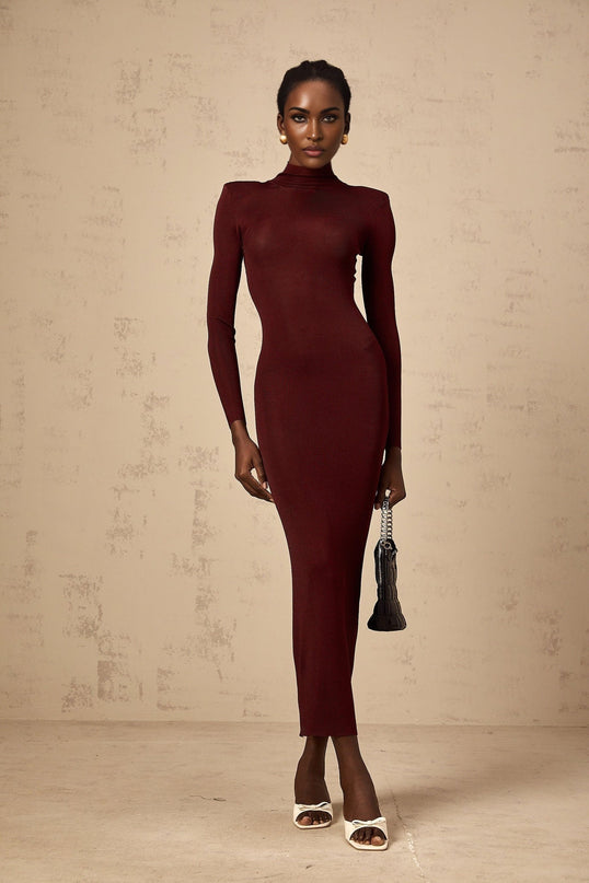 A woman wearing a red semi sheer knitted midi dress with long sleeves standing against a plain background