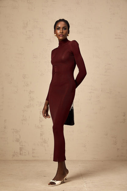 A woman wearing a red semisheer knitted midi dress with long sleeves standing against a plain background