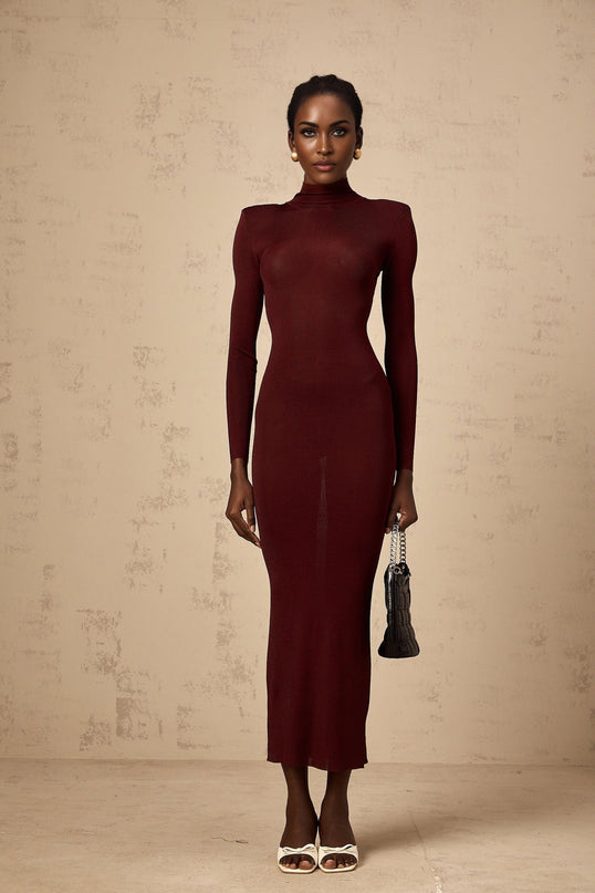 A woman wearing a red semisheer knitted midi dress with long sleeves standing against a plain background