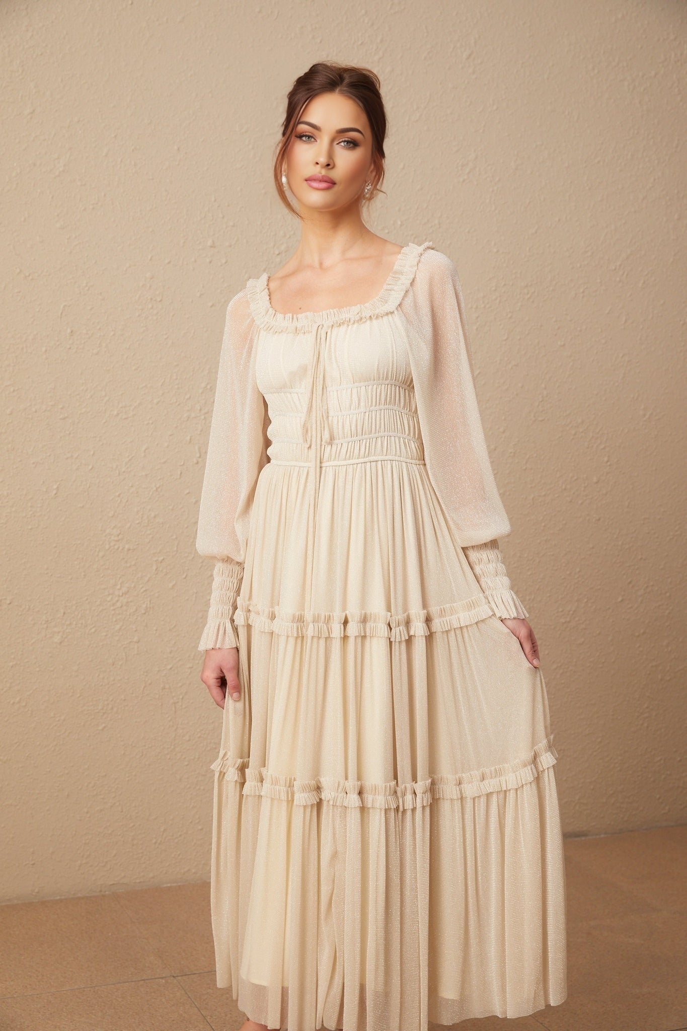 A woman wearing a shimmering metallic midi dress with pleated details and shirred waist standing against a plain background