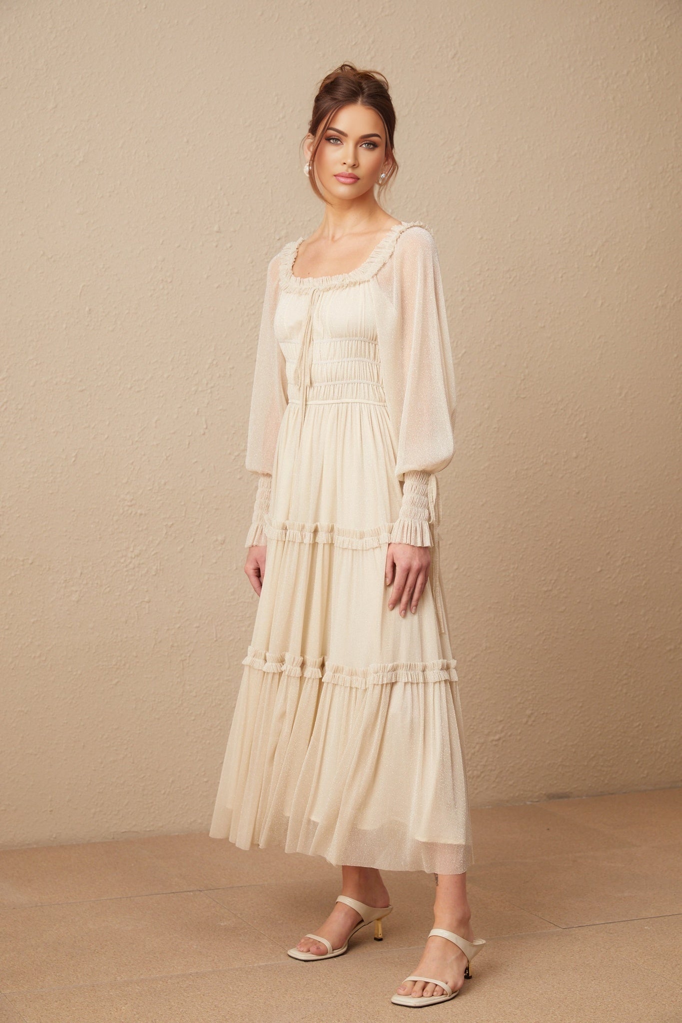 A woman wearing a shimmering metallic midi dress with pleated details and shirred waist standing in an elegant pose