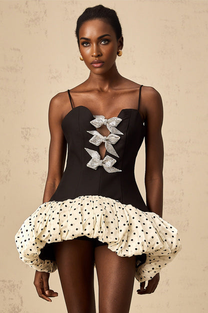 A woman wearing a short colorful dress with polka dots and a large bow accent at the waist The dress features contrasting color blocks and has a playful retro inspired style