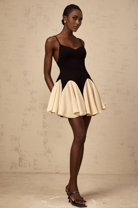 A woman wearing a short dress with colorblocked sections and godet pleats flowing from the waistline creating a flared silhouette