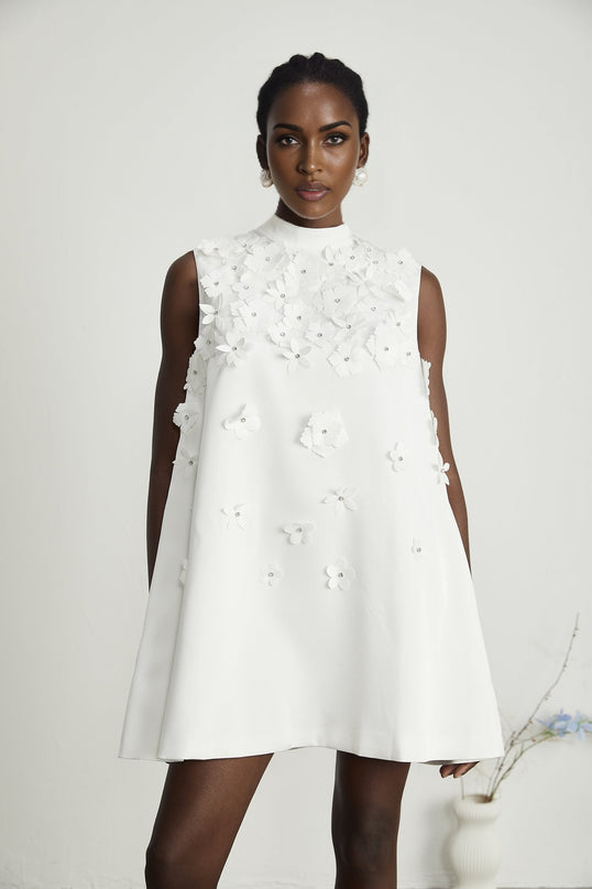 A woman wearing a short floral print dress with a fitted bodice and flared skirt standing against a plain background