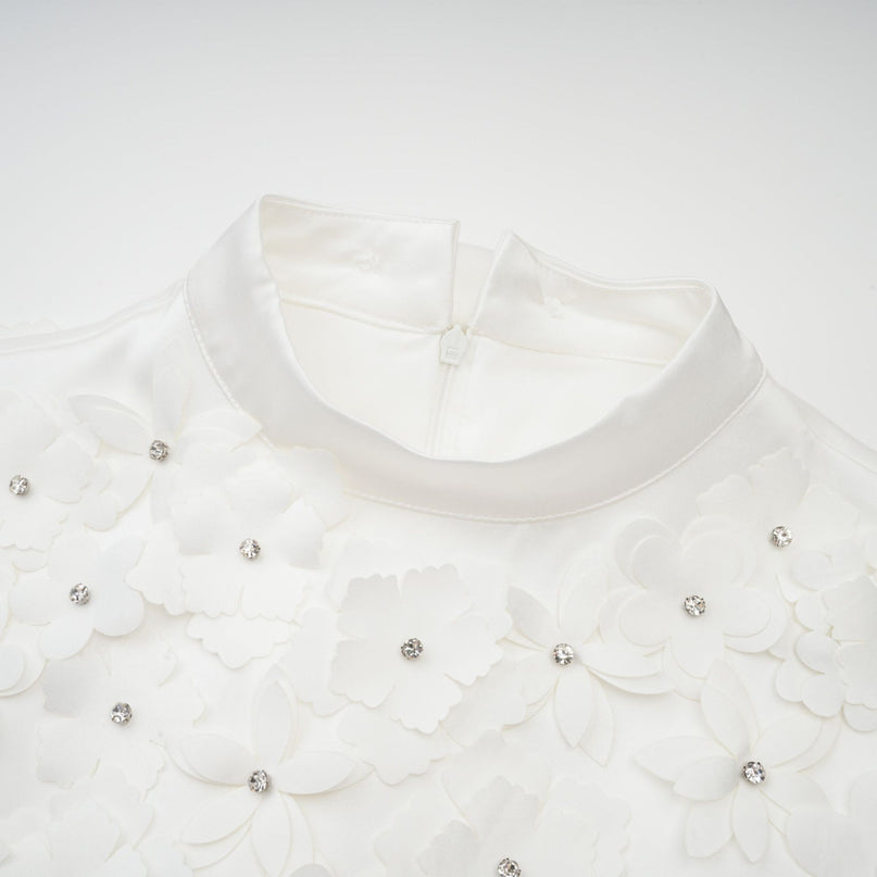 A woman wearing a short floral print dress with puffed sleeves and a fitted waist standing in a relaxed pose against a plain background