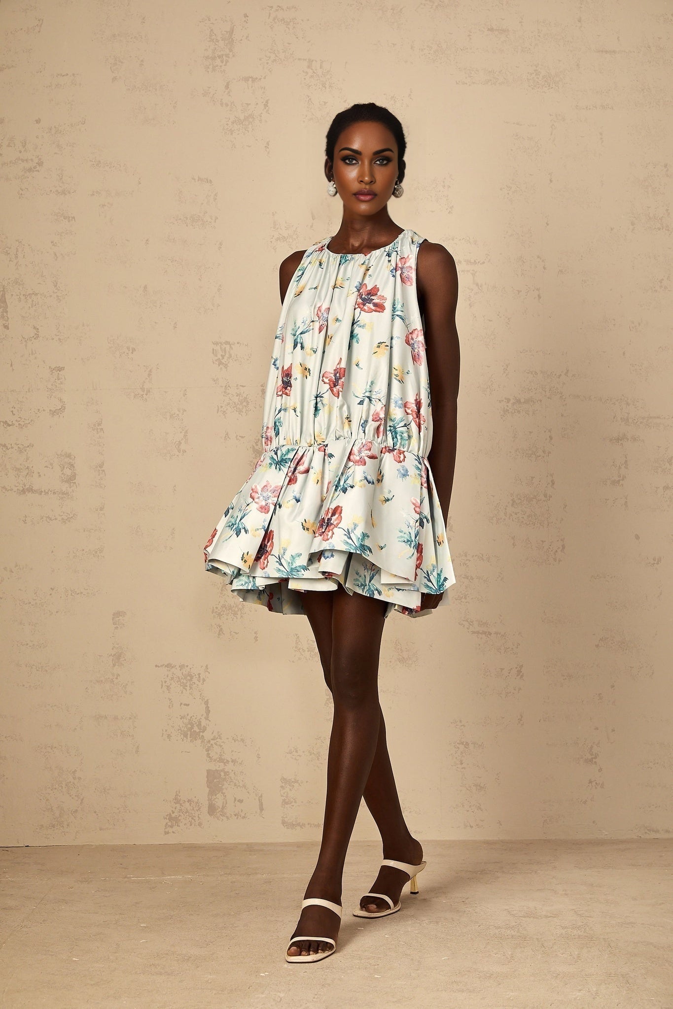 A woman wearing a short green dress with a floral print and shirred details standing in a casual pose