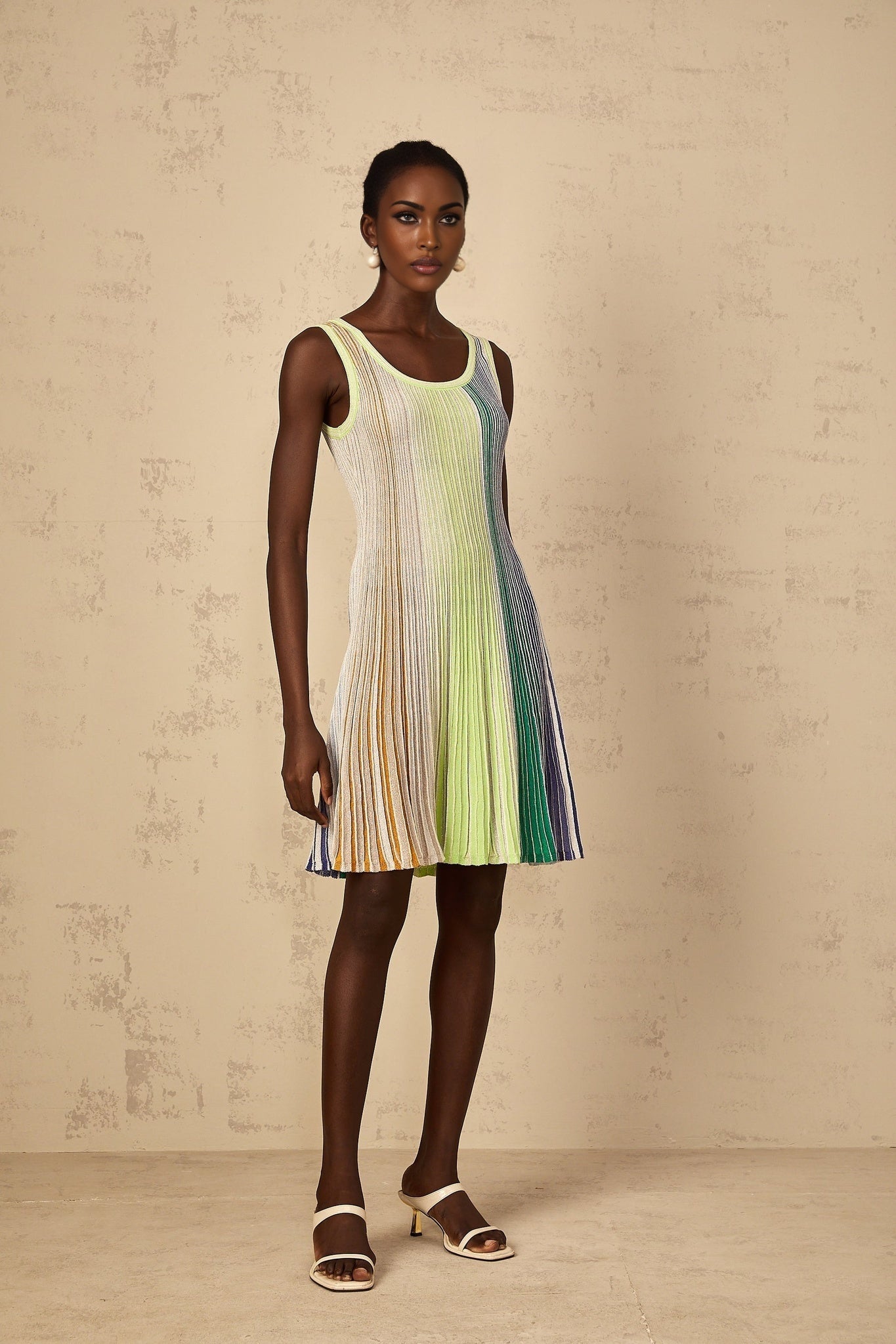 A woman wearing a short green knit dress with sequin stripes standing against a plain background
