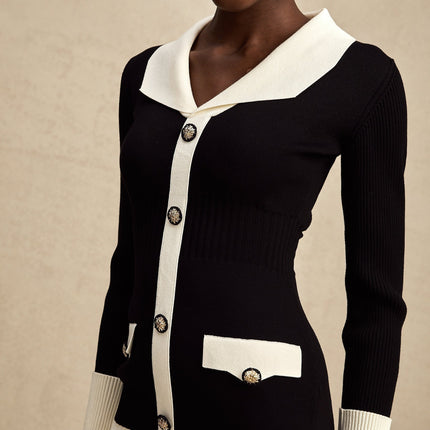 A woman wearing a short knitted dress with ribbed texture featuring color blocks in different shades of wool fabric The dress has long sleeves and a fitted silhouette