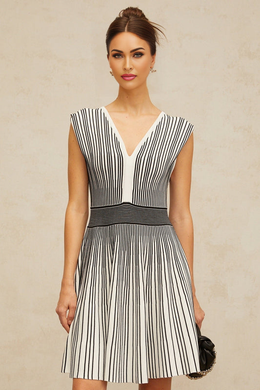 A woman wearing a short knitted dress with vertical stripes in contrasting colors standing against a plain background