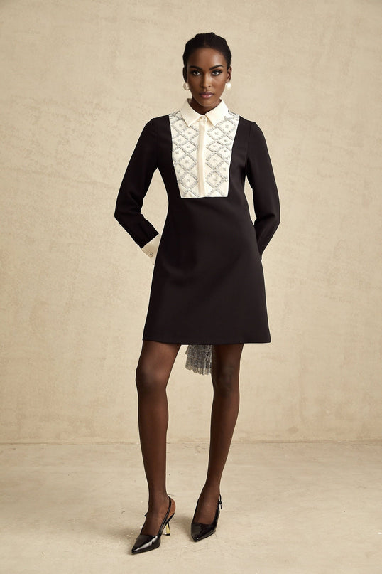 A woman wearing a short mini dress with contrasting colors and embellishments The dress has a fitted silhouette and features decorative details