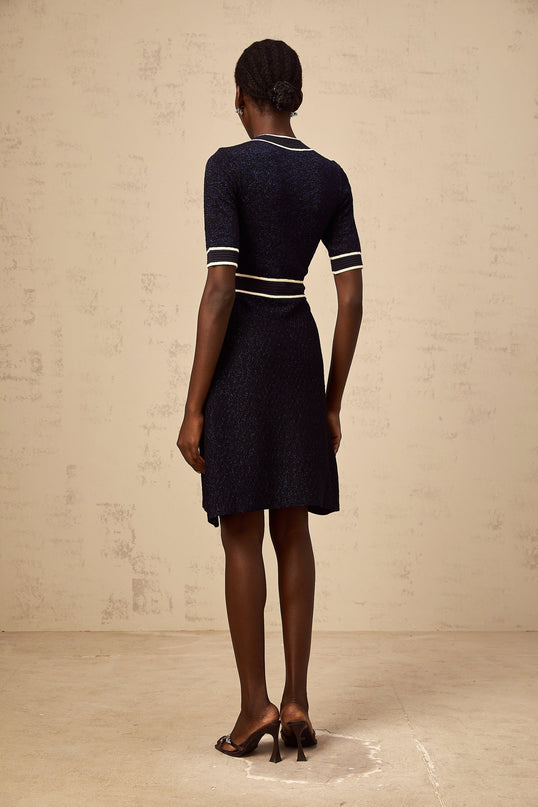 A woman wearing a short navy blue mini dress with glitter knit fabric standing against a plain background