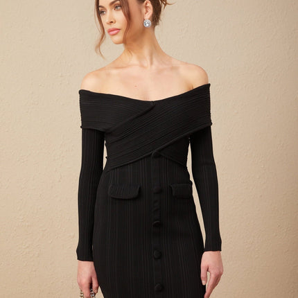 A woman wearing a short offshoulder dress in a ribbed knit fabric The dress is form fitting and has a mini length with long sleeves The model is shown standing in a casual pose
