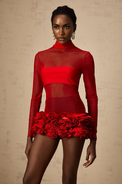 A woman wearing a short red dress with a semisheer tulle overlay featuring threedimensional petal details