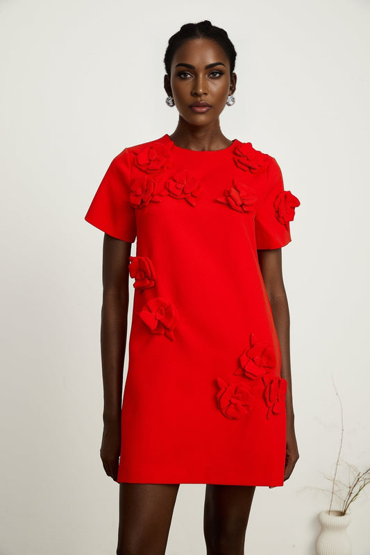 A woman wearing a short red mini dress with floral details and short sleeves standing against a plain background