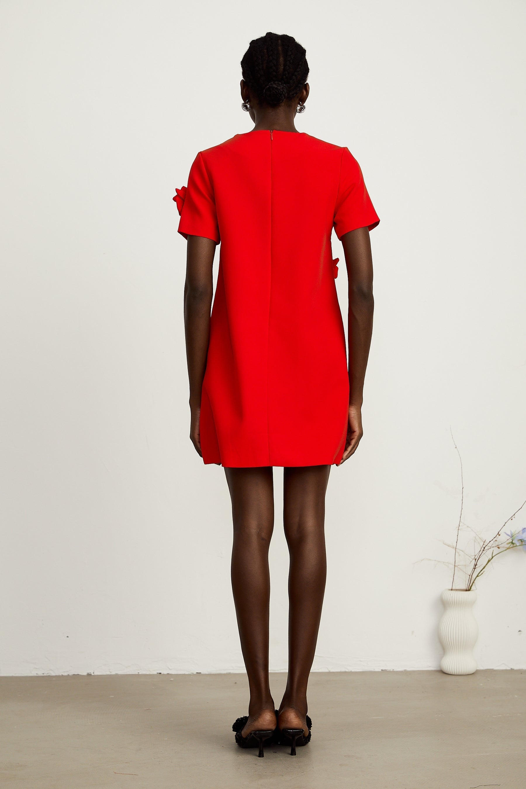 A woman wearing a short red mini dress with floral details and short sleeves standing against a plain background