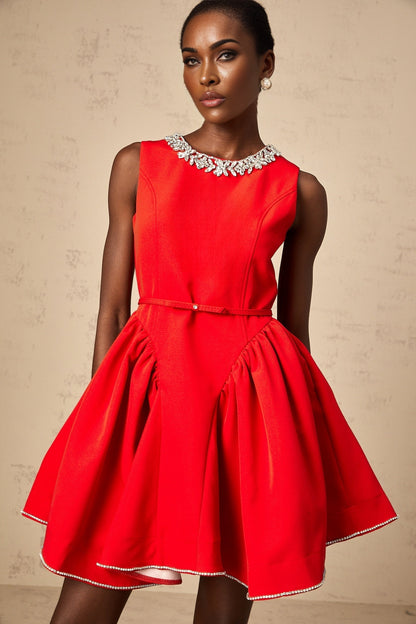 A woman wearing a short red pleated dress with embellishments standing against a plain background