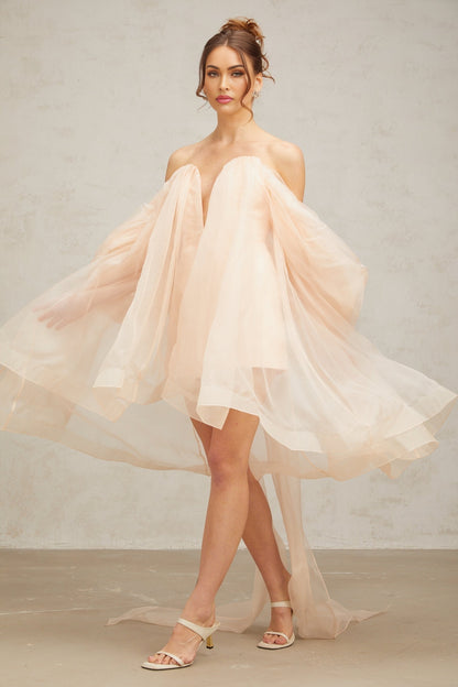 A woman wearing a short voluminous mini dress with a large bow detail at the neckline