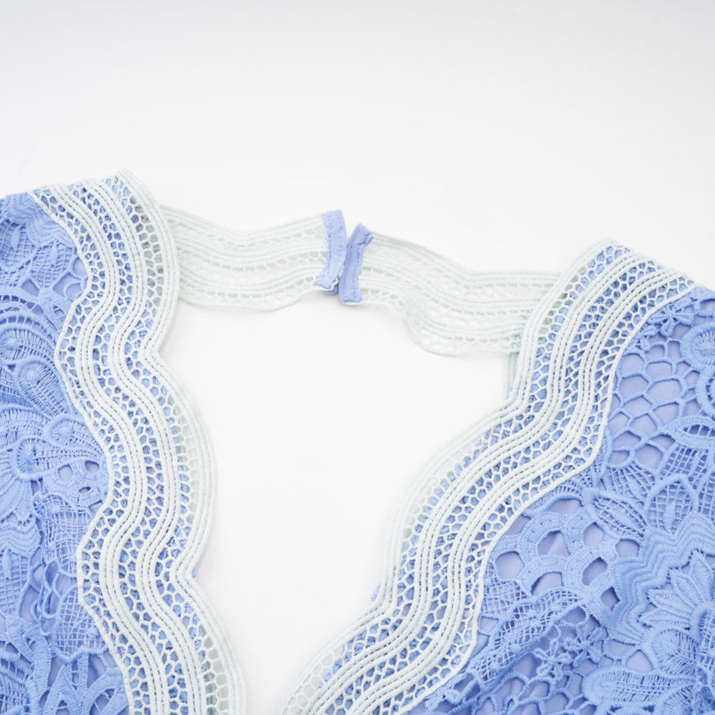 A woman wearing a short white dress with a Vneck and floral embroidery details standing against a plain background