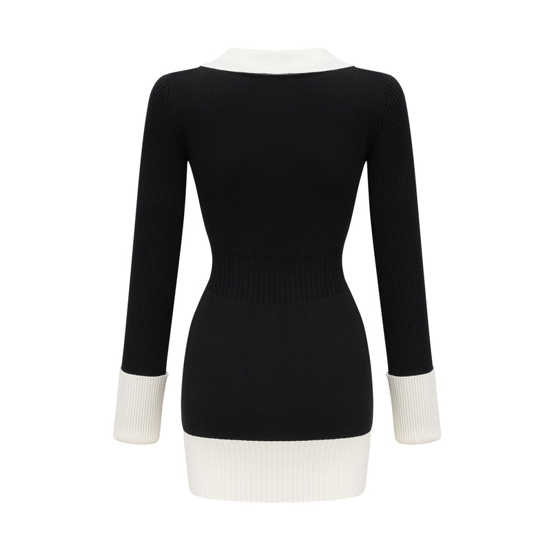 A woman wearing a short wool dress with ribbed knit texture featuring color block design in contrasting shades standing against a plain background