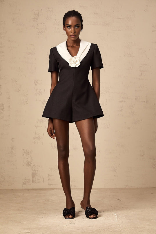 A woman wearing a sleeveless jumpsuit with colorblocked sections and floral appliqués standing in a casual pose