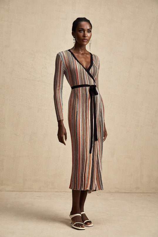 A woman wearing a striped metallic midi dress with a wrap design featuring long sleeves and a v neckline The dress has a shimmery appearance and falls just below the knee