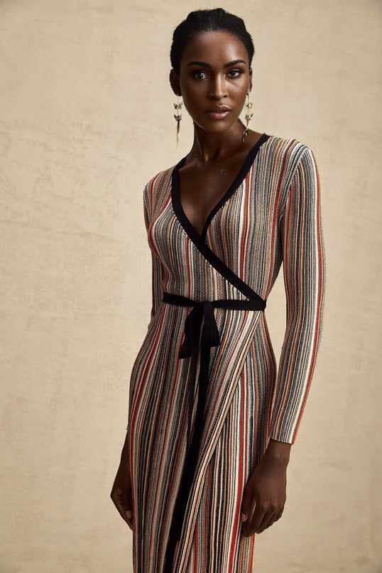 A woman wearing a striped metallic midi dress with a wrap design named Adele The dress features a mix of shimmering stripes and a flattering silhouette that wraps around the body