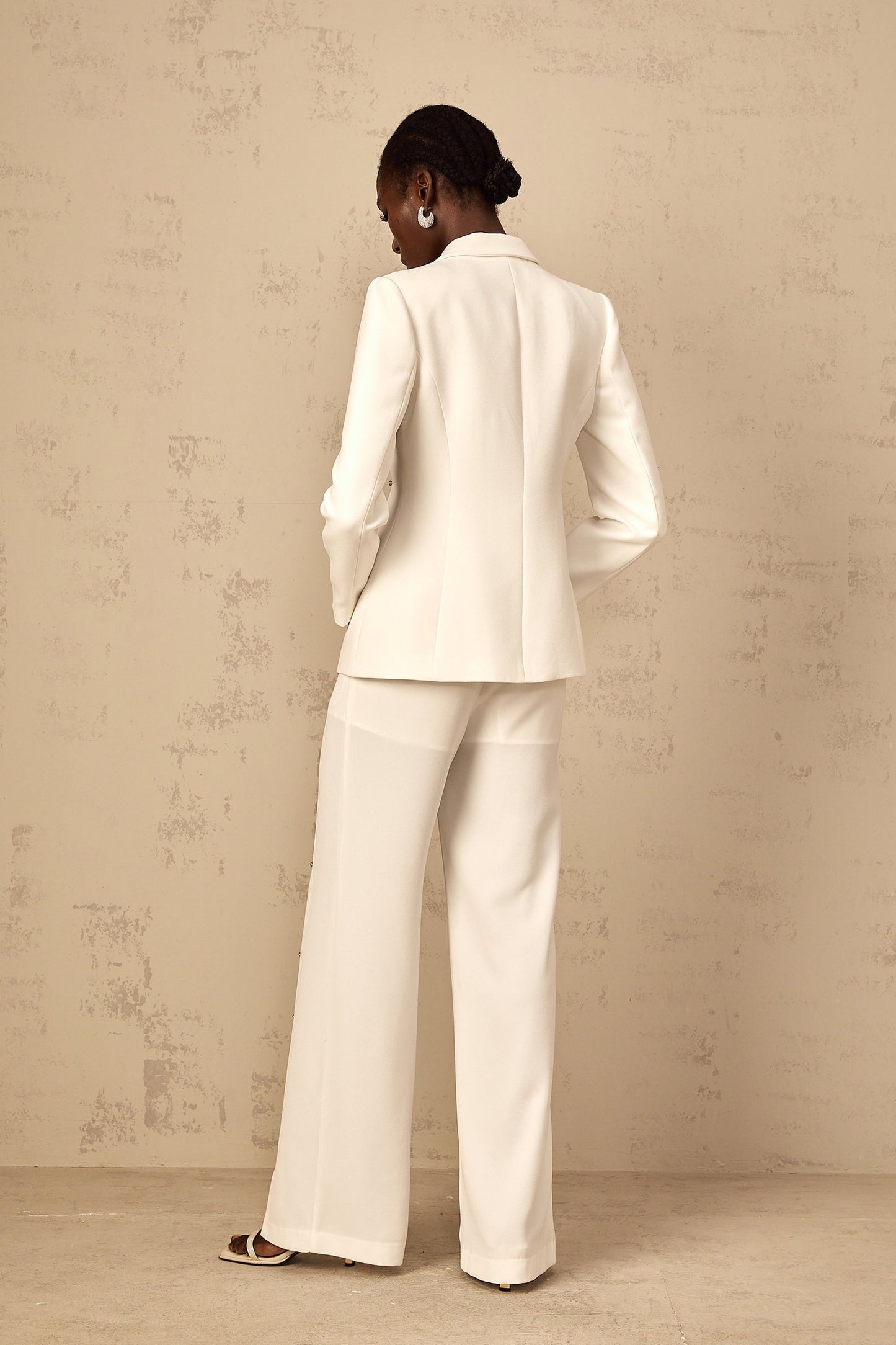 A woman wearing a stylish black blazer and trouser pant set with embellished details on the blazer The outfit is called the Frida set and features a tailored fit