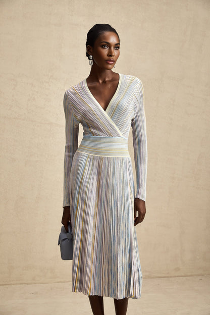 A woman wearing a vertical striped knitted midi dress with long sleeves in multiple colors standing against a plain background